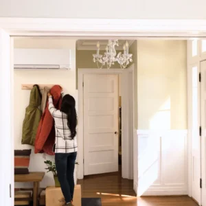 Woman hanging up her winter coat in a home foyer equipped with a wall-mounted ductless mini-split heat pump.
