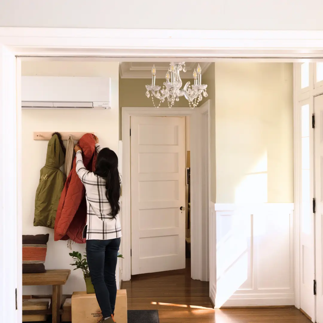Woman hanging up her winter coat in a home foyer equipped with a wall-mounted ductless mini-split heat pump.