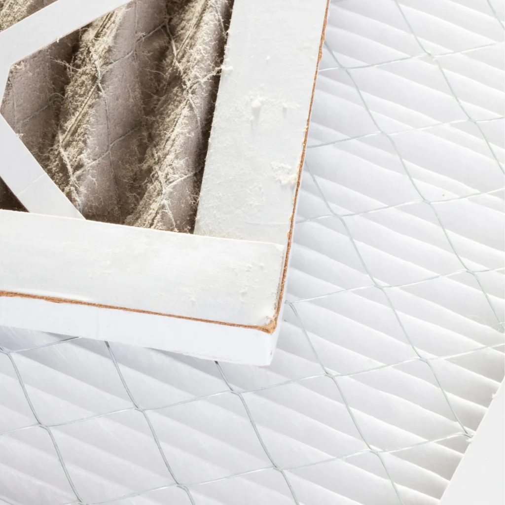 Side by side comparison of a dirty dust clogged air filter sitting on top of a clean white pleated HVAC filter.