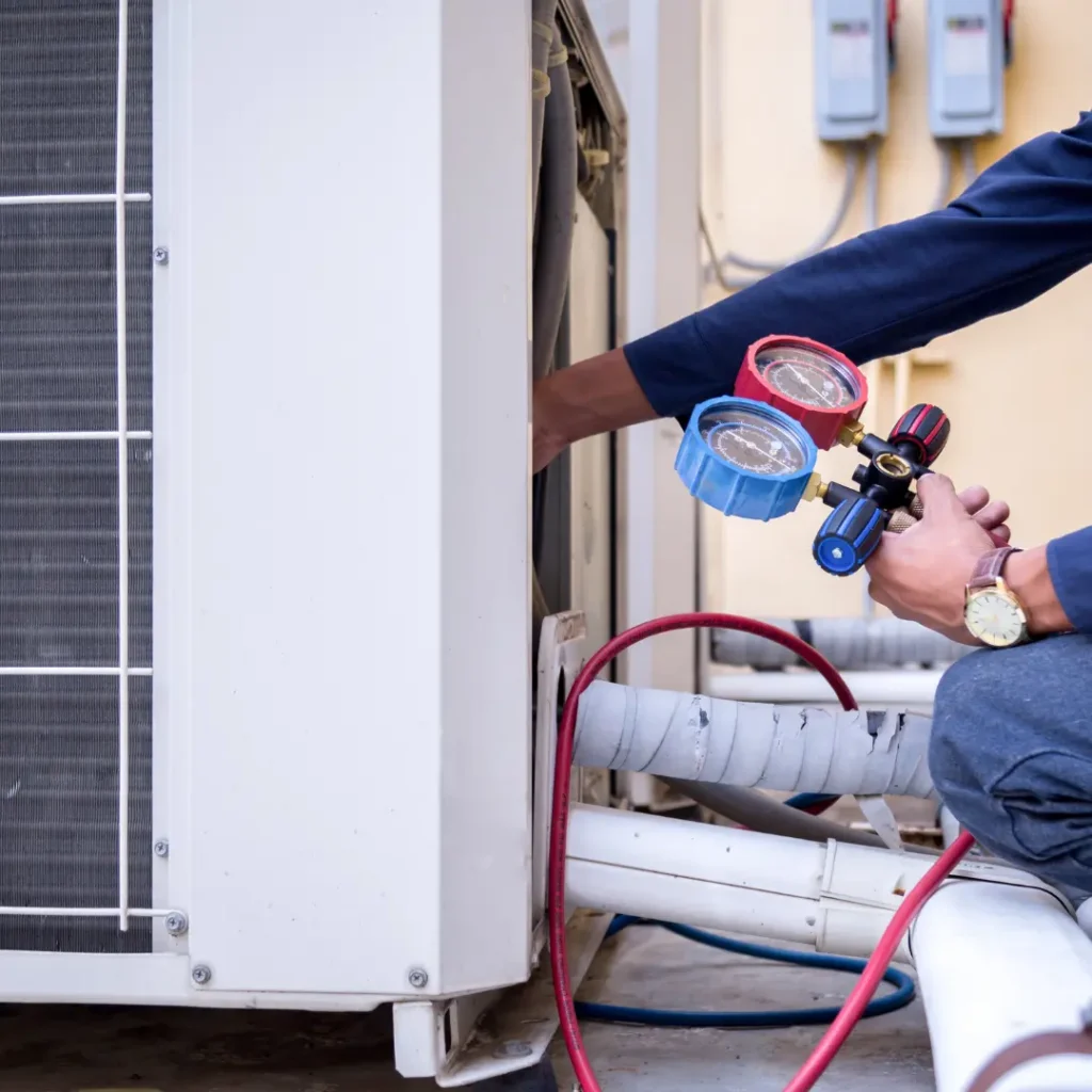 HVAC technician holding pressure gauges while servicing an outdoor air conditioner condenser unit in Northern Virginia.