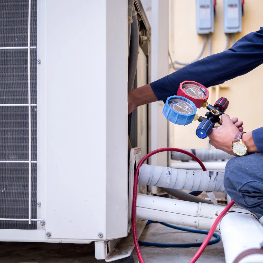 HVAC technician holding pressure gauges while servicing an outdoor air conditioner condenser unit in Northern Virginia.